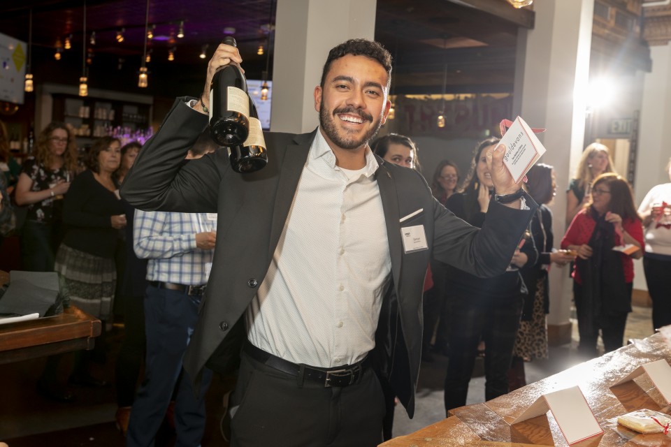 A photo of Samuel Mullin, Marketing Coordinator at Shen Milsom & Wilke LLC, at the SMPS Holiday Party holding two bottles of champagne